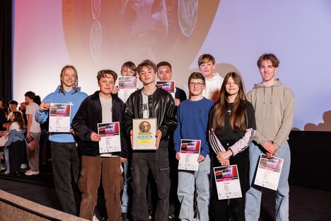 Acht Schüler und eine Schülerin stehen auf der Bühne eines Kinos. Sie halten ihre Urkunden in den Händen.