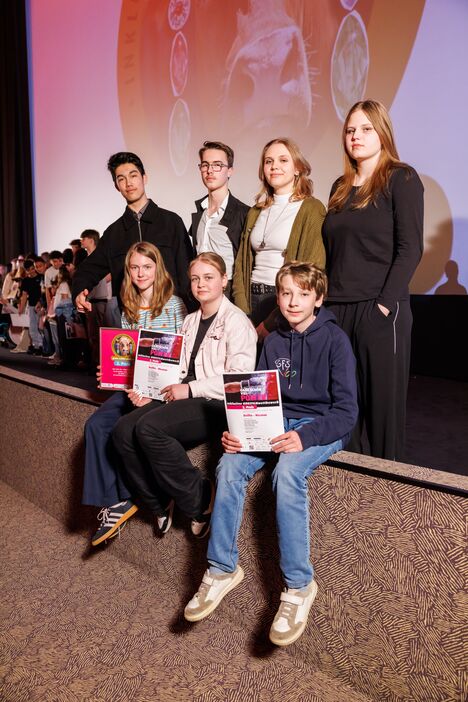 Die Jugendlichen des Filmteams sitzen und stehen auf der Bühne des Astor Kinos in Hannover und halten ihre Urkunden in die Kamera.