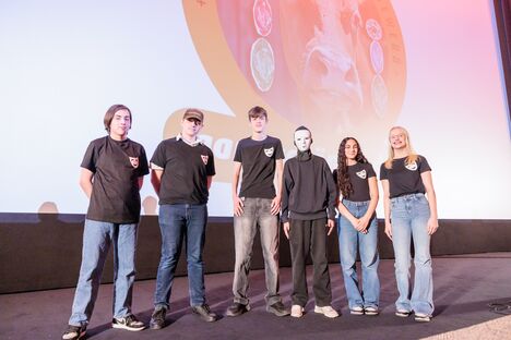 Sechs Schüler*innen stehen auf der Bühne des Astor Kinos und blicken in die Kamera. Ein Schüler hat eine Maske auf.